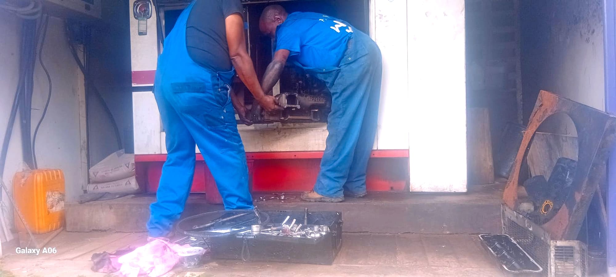 Two EmersonEIMS technicians overhauling the St Austin Academy 50 kVA Perkins generator engine on site, with the Perkins engine and an open tool kit visible