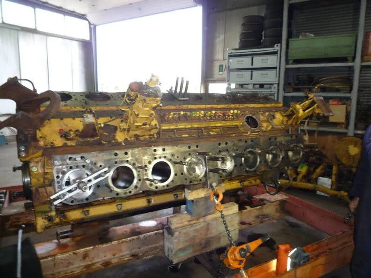 Large diesel engine block stripped to the bare casting and supported on timber and lifting gear in the EmersonEIMS workshop