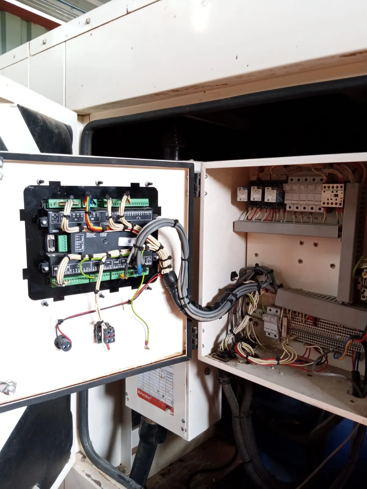 Open control box on a second canopy generator showing the controller rear, relays, fuses and terminals