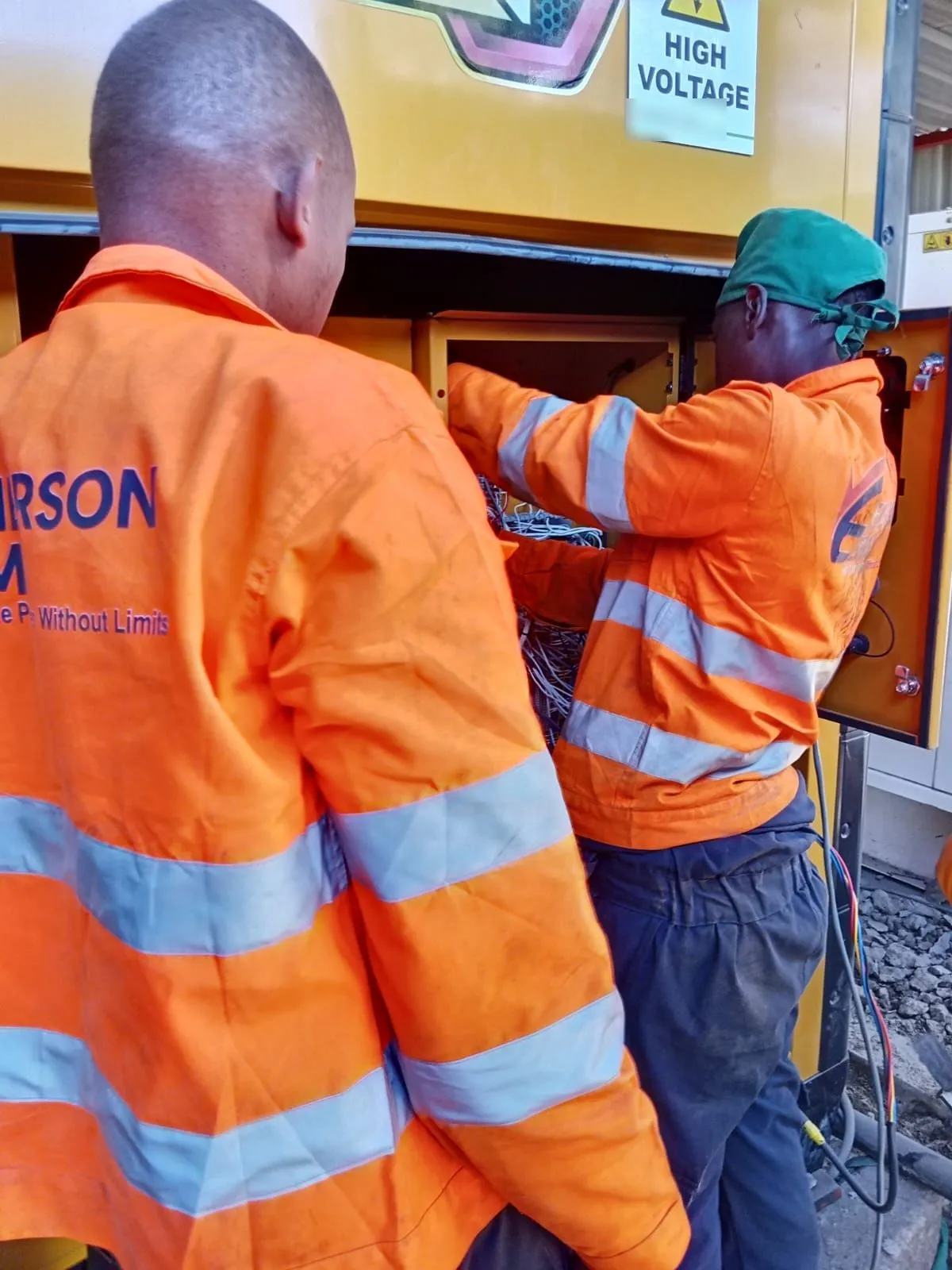 Two EmersonEIMS technicians in branded hi-vis working at a CAT generator control panel