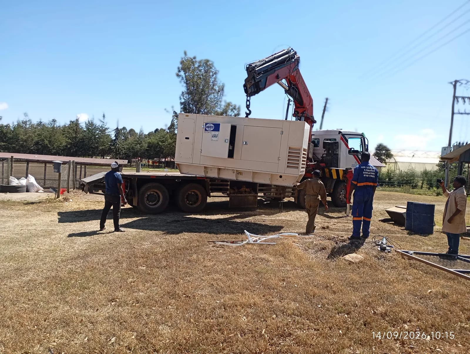 Crane truck lifting a canopy generator onto a flatbed while the team guides it
