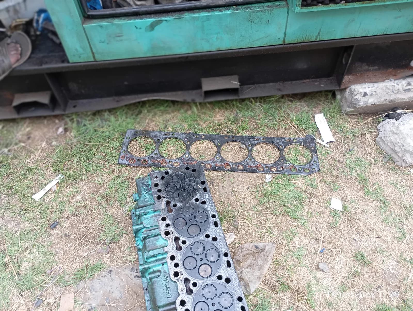 Cylinder head and old head gasket laid out beside a generator during an engine overhaul