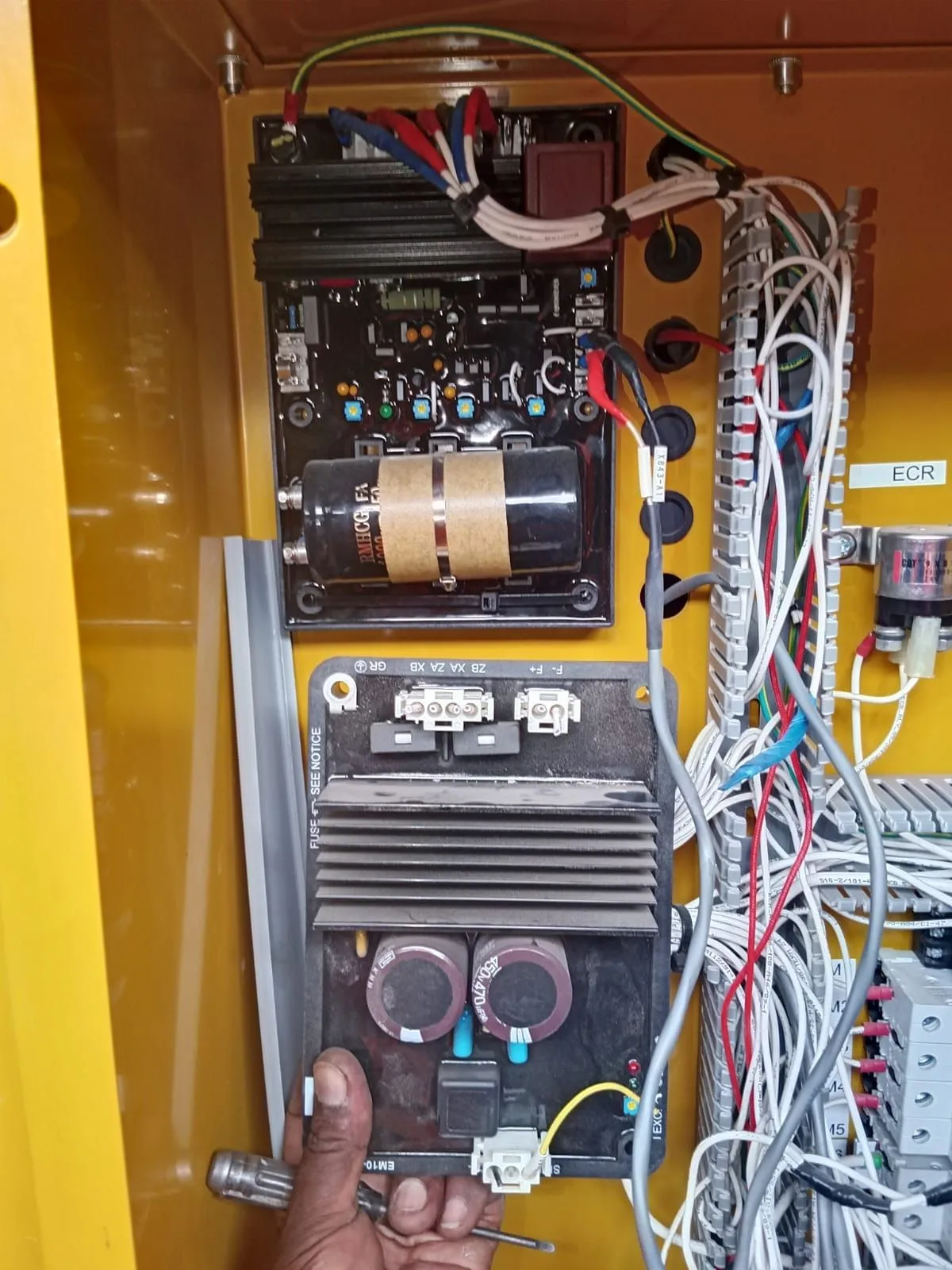 Technician working on the AVR and excitation module inside a generator terminal box