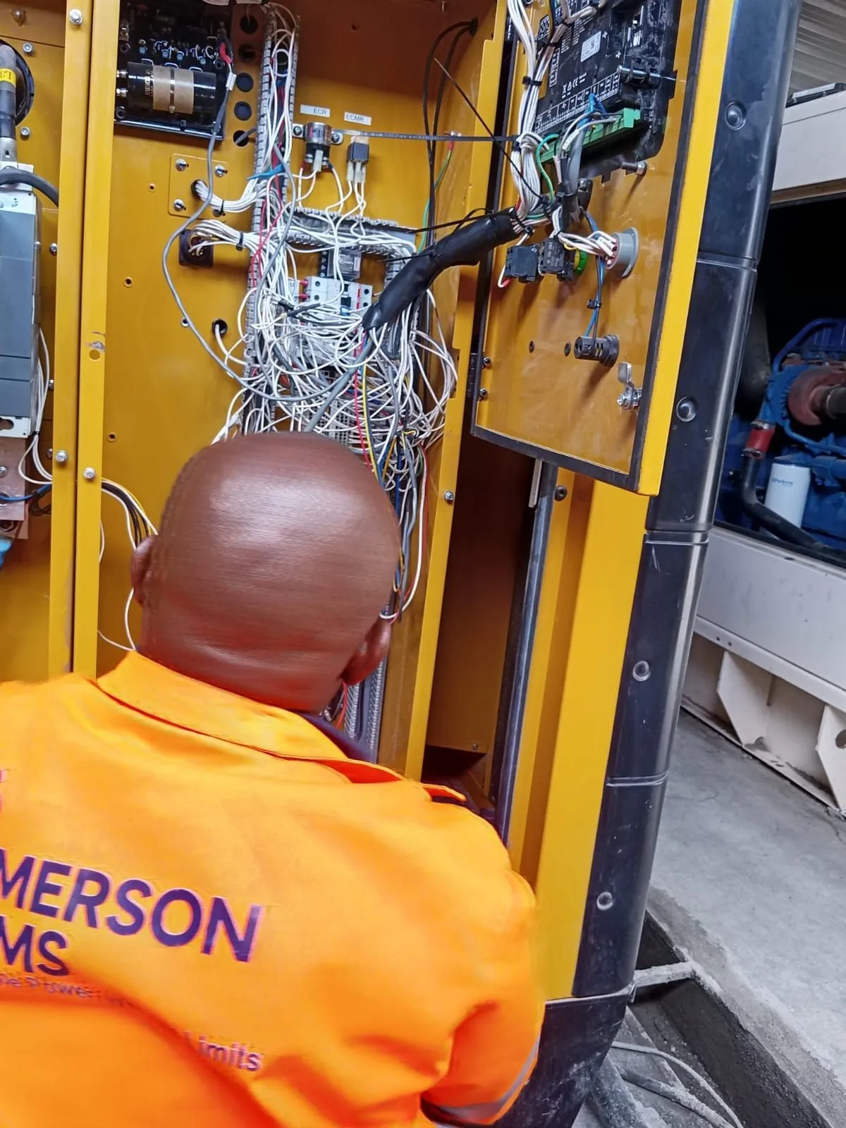 EmersonEIMS technician tracing control wiring inside a generator cabinet