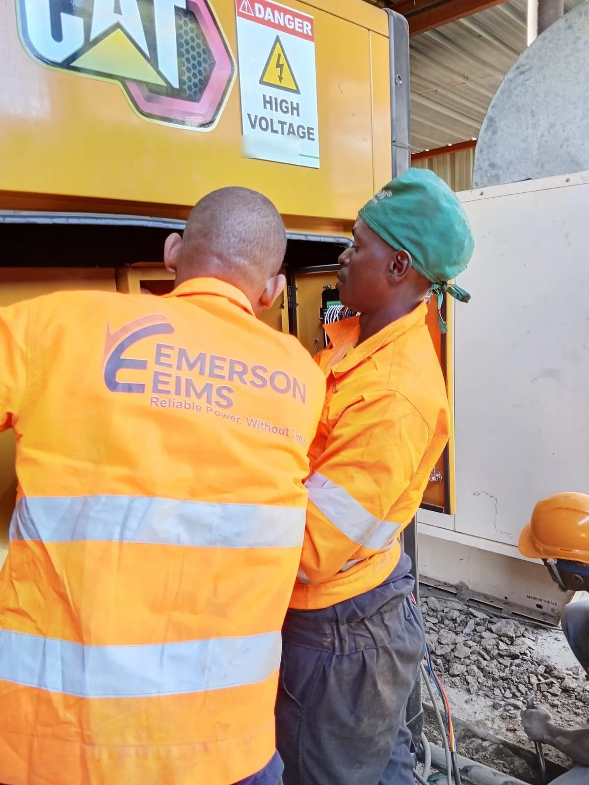 Two EmersonEIMS technicians at a CAT generator, the company logo on the hi-vis jacket