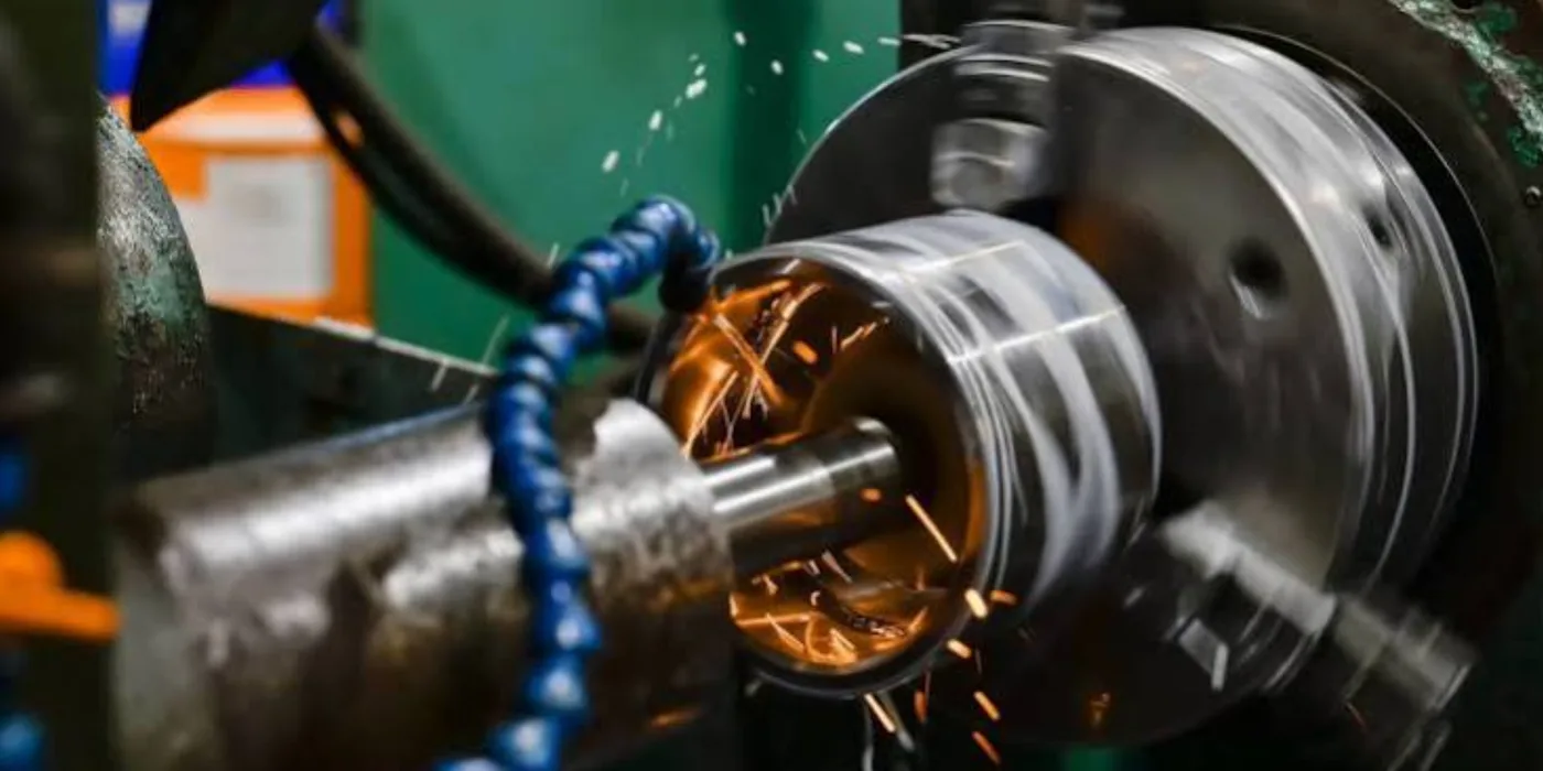 Precision cylindrical grinding of a shaft on a machine tool in the EmersonEIMS workshop, with coolant and sparks