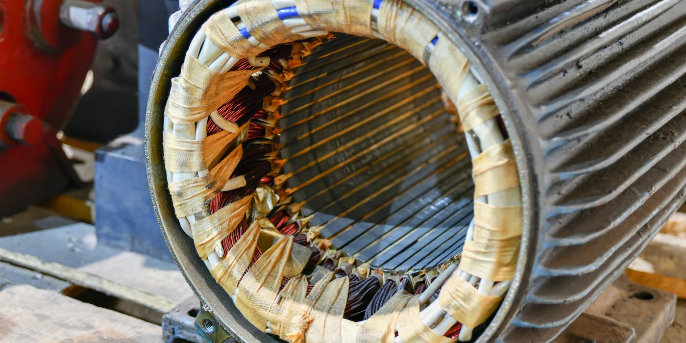 Three-phase stator freshly rewound with copper windings laced and taped, showing the core laminations and slot insulation