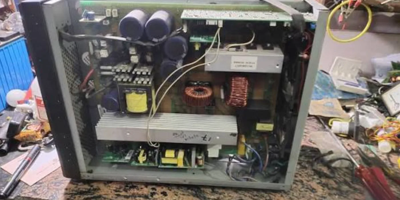 Online UPS opened on the bench showing DC-bus capacitors, power-stage heatsink, toroidal chokes and control boards during diagnosis at EmersonEIMS